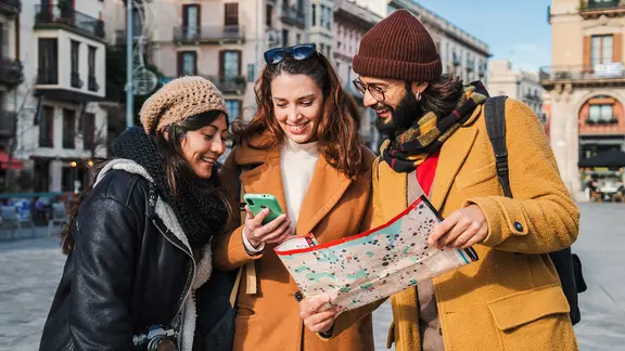 Zwei Frauen und ein Mann haben einen Stadtplan und blicken zusammen ins Handy.