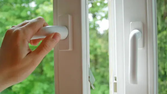 Eine Hand öffnet ein Fenster.
