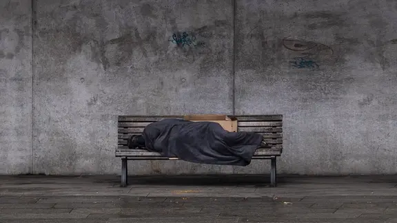 Wie viele Menschen in Rostock wohnungs- und obdachlos sind, soll im Rahmen einer europäischen Studie herausgefunden werden. (Themenbild) | IMAGO / photothek Ein Obdachloser schläft auf einer Bank.