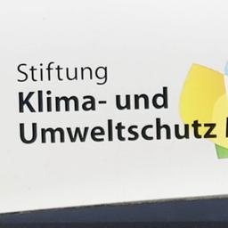 Das Foto zeigt den Schriftzug "Stiftung Klima- und Umweltschutz MV" und ein gelb-blau-grünes Singnet auf weißem Grund.