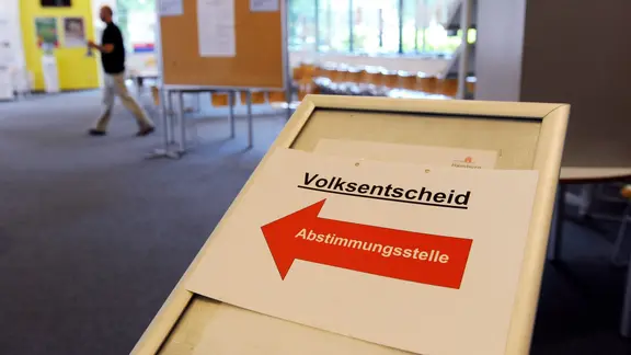 Ein Schild mit einem Volksbegehren steht an einem Wahllokal in Hamburg. 