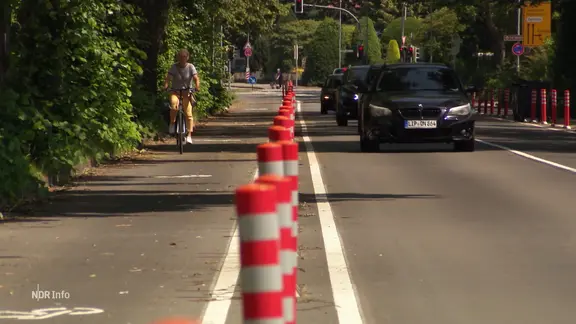 Eine Fahrradfahrerin fährt neben Autos auf der Straße.