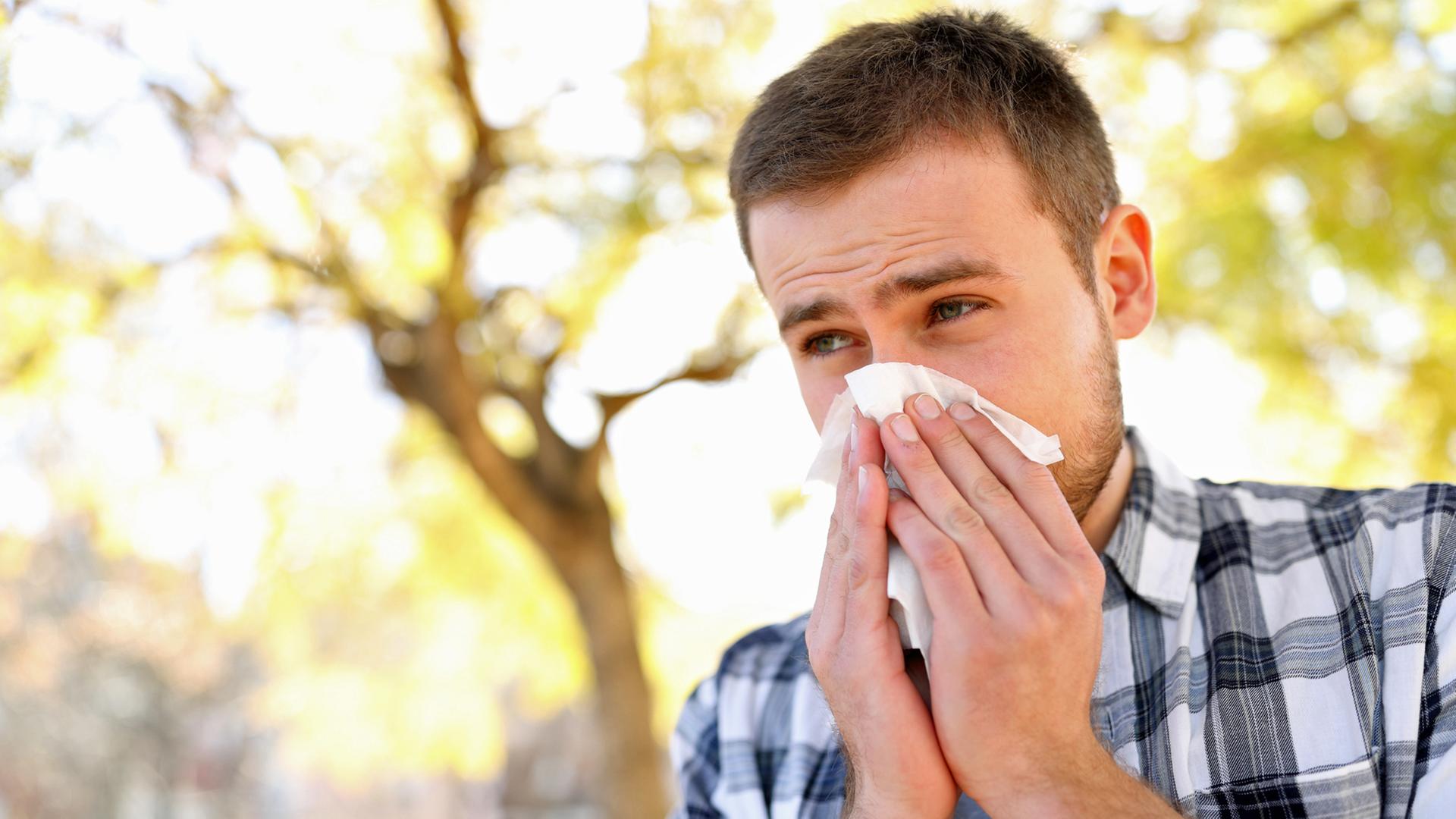 Ein Mann schneuzt sich im Freien die Nase mit einem Taschentuch. | colourbox