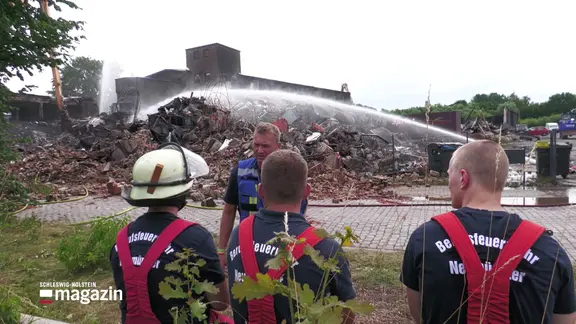 Feuerwehrleute bei Löscharbeiten vor einer abgebrannten Halle