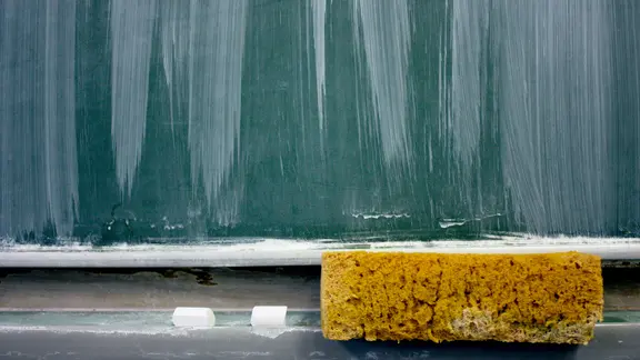 Eine Schultafel, darunter ein Schwamm und Kreide.