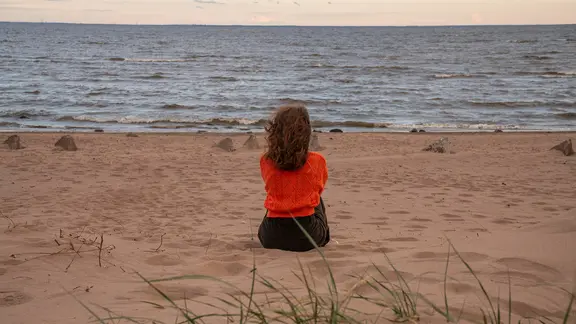 Eine Frau, von hinten gesehen, sitzt am Strand