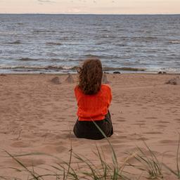 Eine Frau, von hinten gesehen, sitzt am Strand