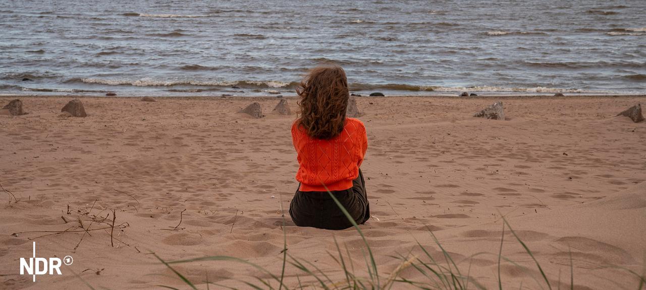 Eine Frau, von hinten gesehen, sitzt am Strand