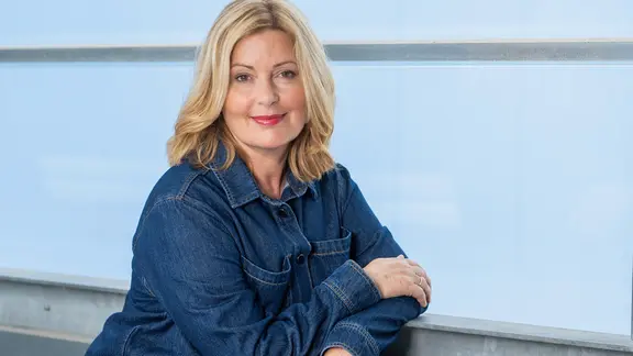 Karin Thaler lehnt an einem Geländer und lächelt in die Kamera. 