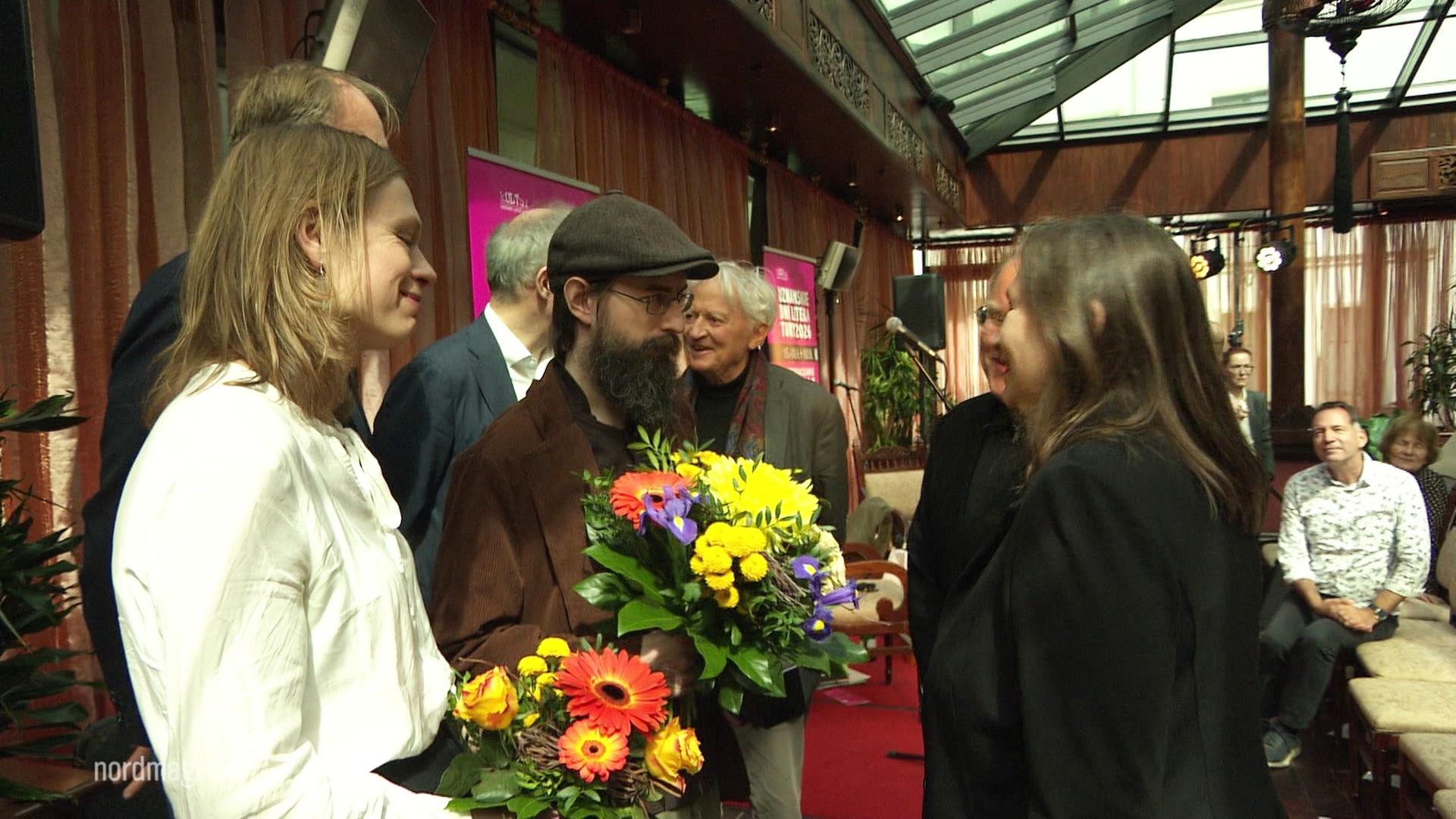 Clemens J. Setz mit einem Blumenstrauß, umringt von mehreren Personen. | Screenshot