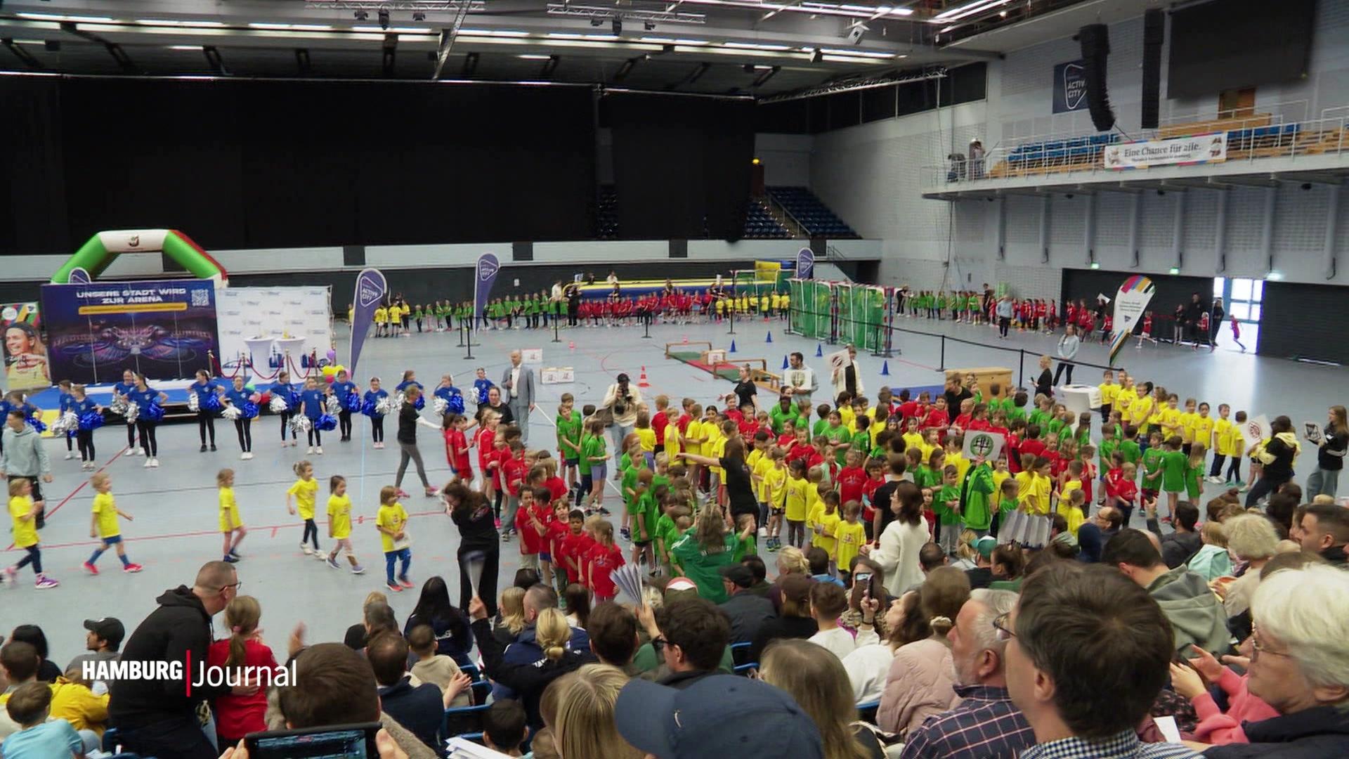 Viele Kinder stehen in grünen, gelben und roten Shirts in einer Sporthalle. | Screenshot