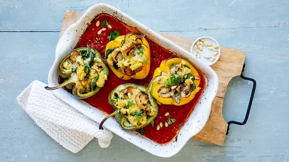 Eine Auflaufform mit gefüllten Paprikahälften in einer Tomatensoße. 