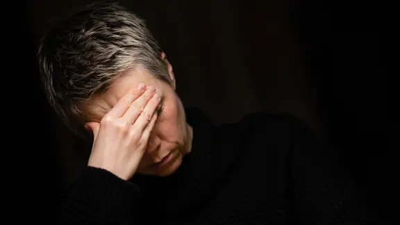 Eine Frau sitzt hält sich die Hände vor das Gesicht.