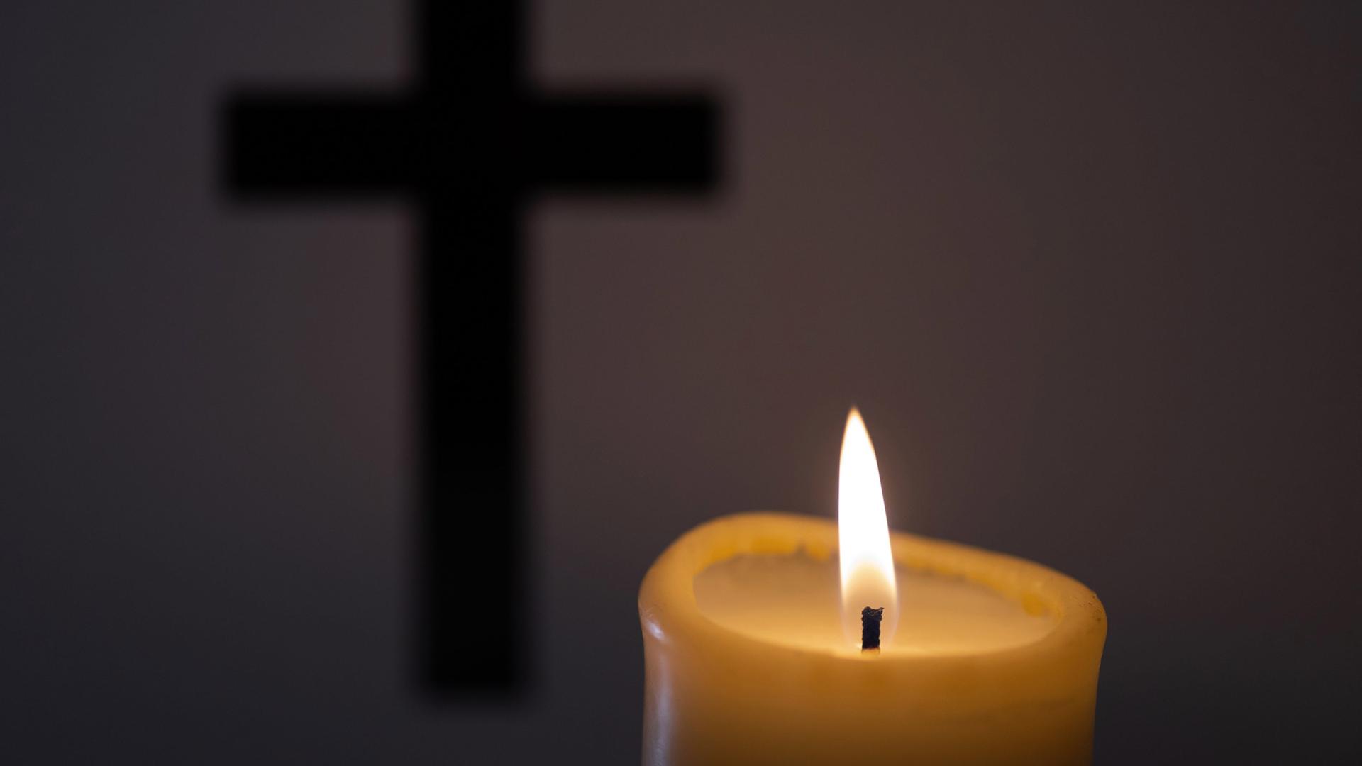 Eine Kerze brennt vor einem Kreuz | picture alliance / Andreas Franke