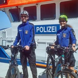 Uniformierte Polizisten im Bäderdienst stehen mit Fahrrädern vor einem Polizeischiff.