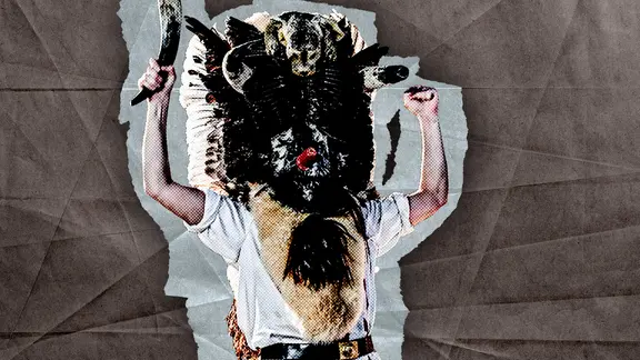 Bild des Klaasohm. Ein Mann mit einer traditionellen Maske, aus Federn, Tieren und einem Kuhhorn in der Hand. Er streckt die Arme in die Luft. Sein Gesicht ist nicht zu sehen.