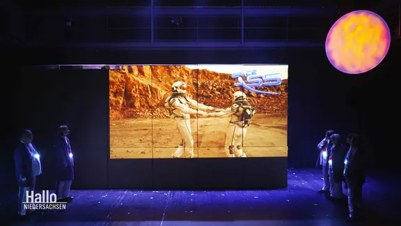 Bei einer Theateraufführung wird ein tanzendes Astronauten-Paar auf einer Leinwand projiziert.