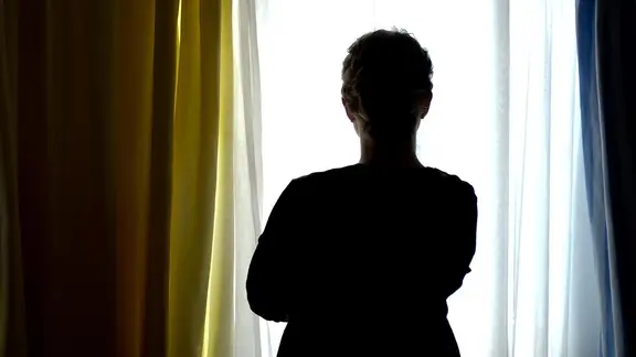 Eine junge Frau steht in einem Zimmer am Fenster.