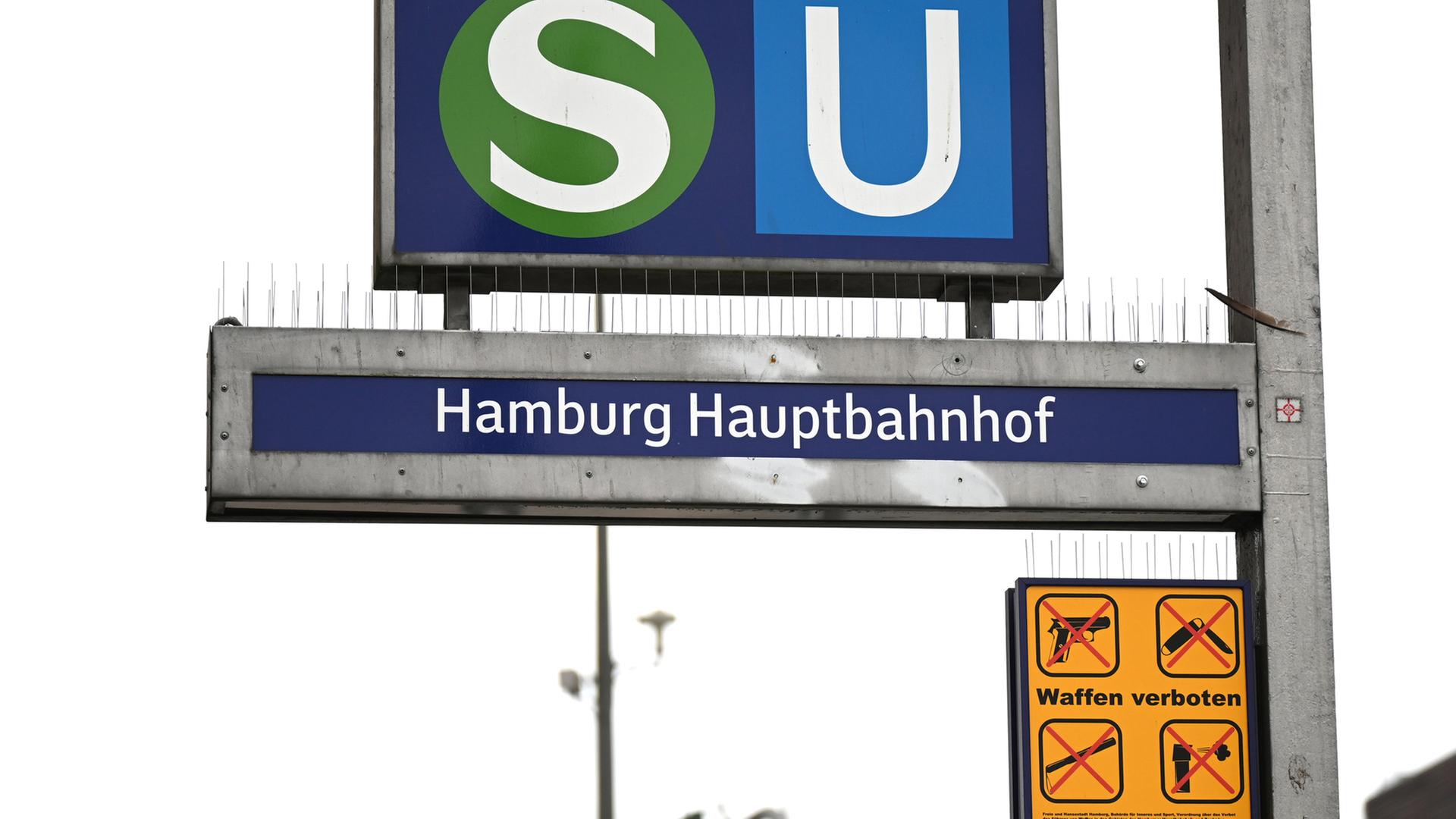 Ein gelbes Schild, das auf das geltende Waffenverbot hinweist, hängt unter dem Eingangsschild am Hamburger Hauptbahnhof neben den Logos von S-Bahn und U-Bahn. | picture alliance/dpa, Niklas Graeber