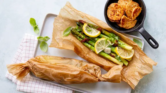 In Pergamentpapier eingeschlagener grüner Spargel, daneben einige Scheiben Tempeh.