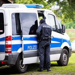 Ein Polizist steht am 13. Juni 2024 während einer Razzia auf einem Hof bei Espelkamp an einem Einsatzfahrzeug.