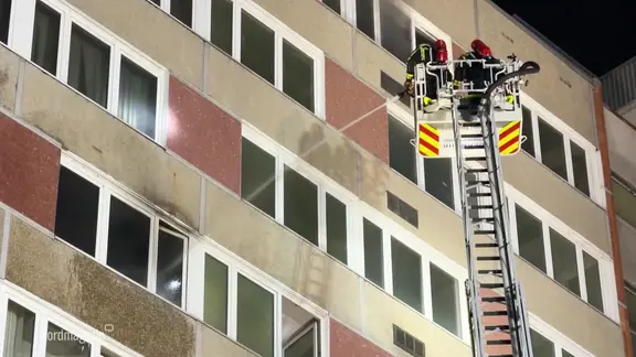 Feuerwehrmänner halten einen Löschstrahl auf ein rußieges Haus.