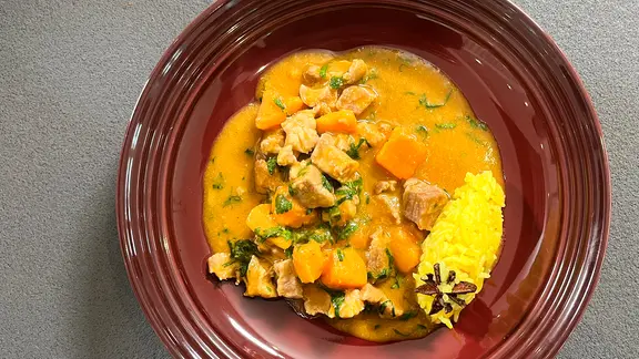 Schweinefleischcurry mit Süßkartoffeln auf einem braunen Teller angerichtet