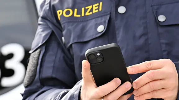Ein Polizist tippt auf ein Smartphone.