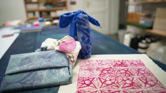 Verschiedene in Stoff eingepackte Geschenke liegen auf dem Tisch eines Ateliers. 