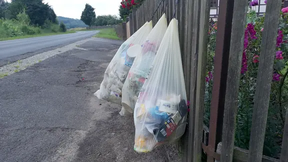 An einem Zaun hängen Müllsäcke.