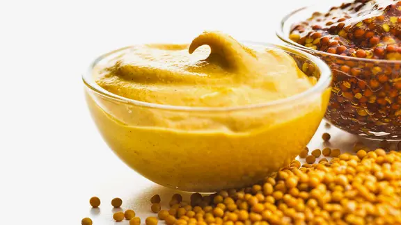 Eine Glaschüssel mit Senf, daneben liegen Senfkörner.