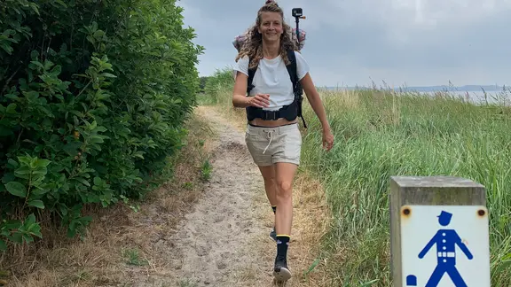 Eine junge Frau mit Rucksack wandert auf einem Küstenweg.