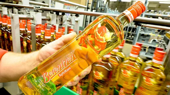 Ein Mitarbeiter der Firma Berentzen hält eine Flasche Apfelkorn in der Hand.