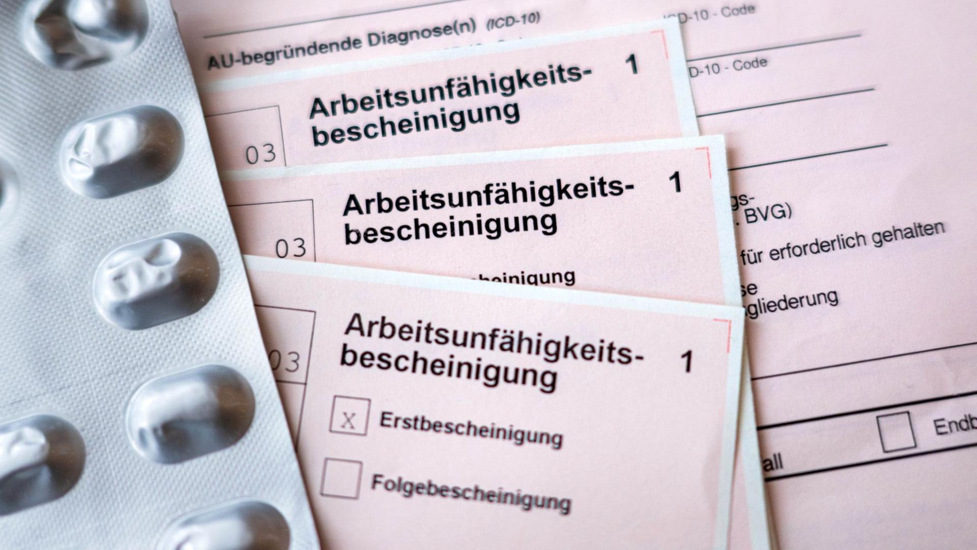 Krankenscheine und ein Medikamentenblister liegen auf einem Tisch. (Themenbild) | Sina Schuldt/dpa 