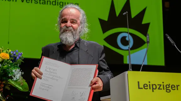 Miljenko Jergović nació en 1966 en Sarajevo. Internacionalmente es conocido por su colección de cuentos "Sarajevo Marlboro". | picture alliance/dpa | Hendrik Schmidt El escritor croata-bosnio Miljenko Jergović sostiene un certificado en alto y sonríe