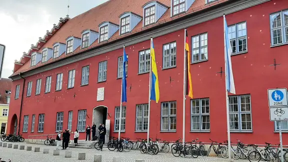 Der Haupteingang der Greifswalder Rathauses, davor stehen Fahrräder, einige Fahnen wehen vor dem Gebäude
