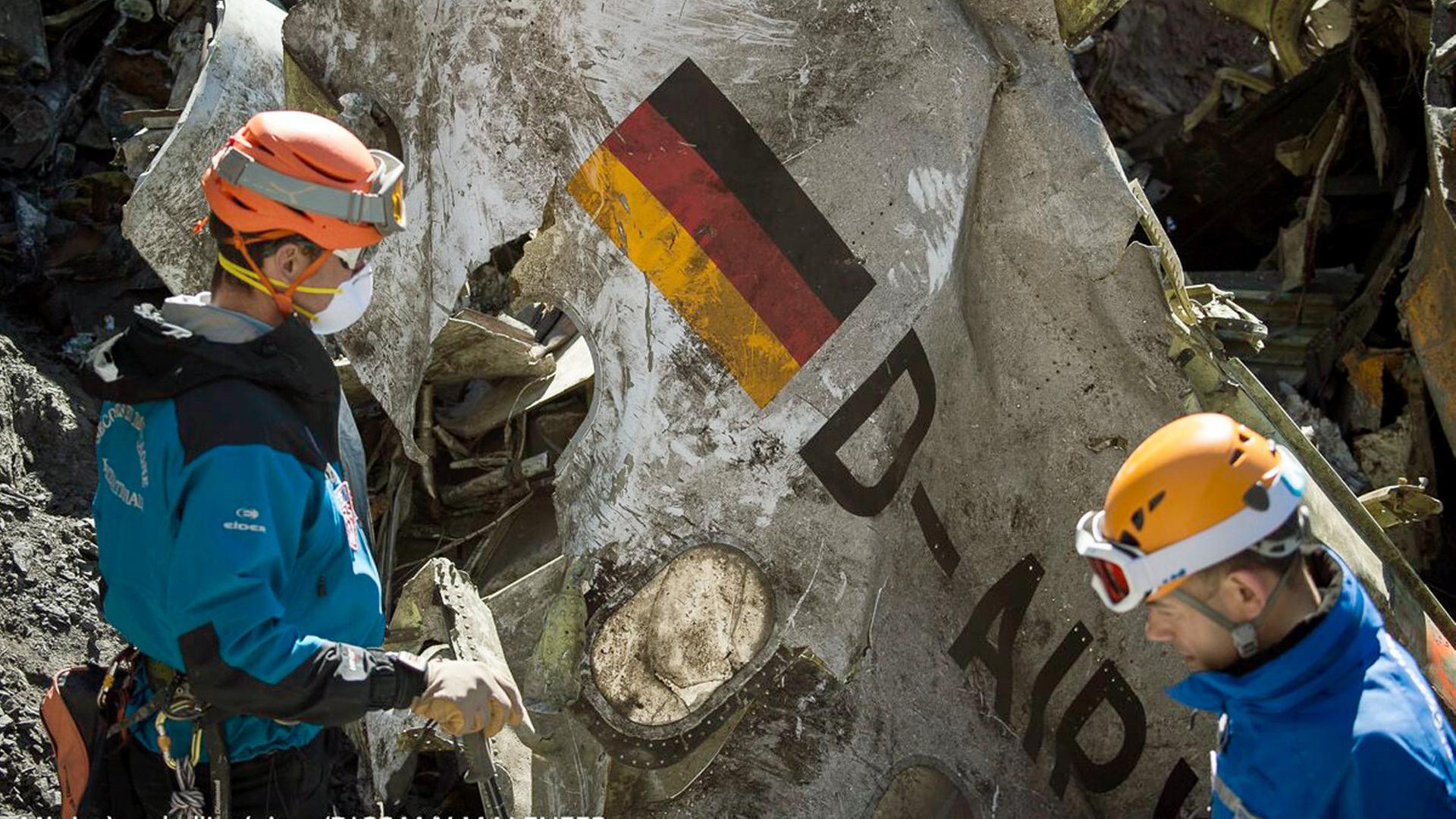 Zwei Bergungskräfte stehen vor einem Wrackteil eines Flugzeugs. | picture alliance / dpa | Yves Malenfer/Dicom/Ministere In