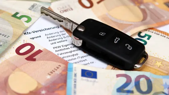 Ein Autoschlüssel liegt auf Euroscheinen. Es ist ein Dokument zu sehen, auf dem Kfz-Versicherung steht.