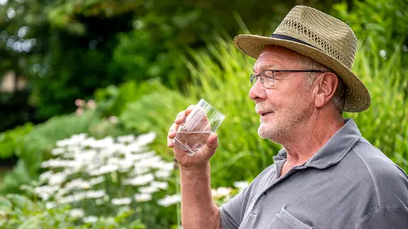 Ein älterer Mann mit Sonnenhut hält ein Glas Wasser in der Hand.