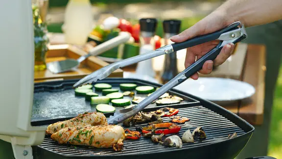 Auf einem Grillrost werden Gemüsestücke und Hähnchenbrust gegrillt.
