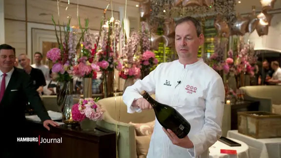 Küchenchef Christoph Rüffer öffnet eine Flasche Champagner.
