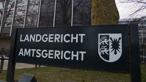 Ein schwarzes Schild mit dem Schriftzug "Landgericht Amtsgericht" steht vor dem Gebäude des Land- und Amtgerichts in Lübeck.