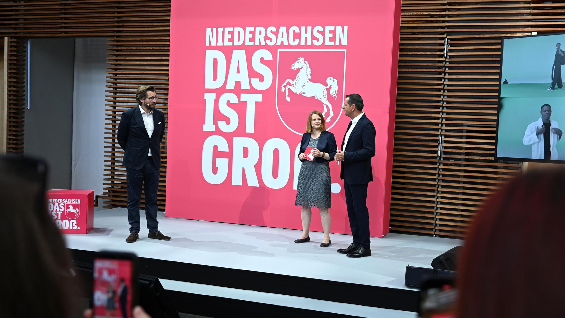 Menschen stehen auf einer Bühne vor dem neuen Slogan 