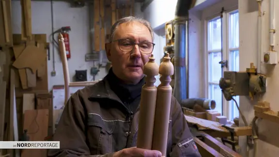 Ein Mann mit zwei Holzteilen in einer Tischlerei.