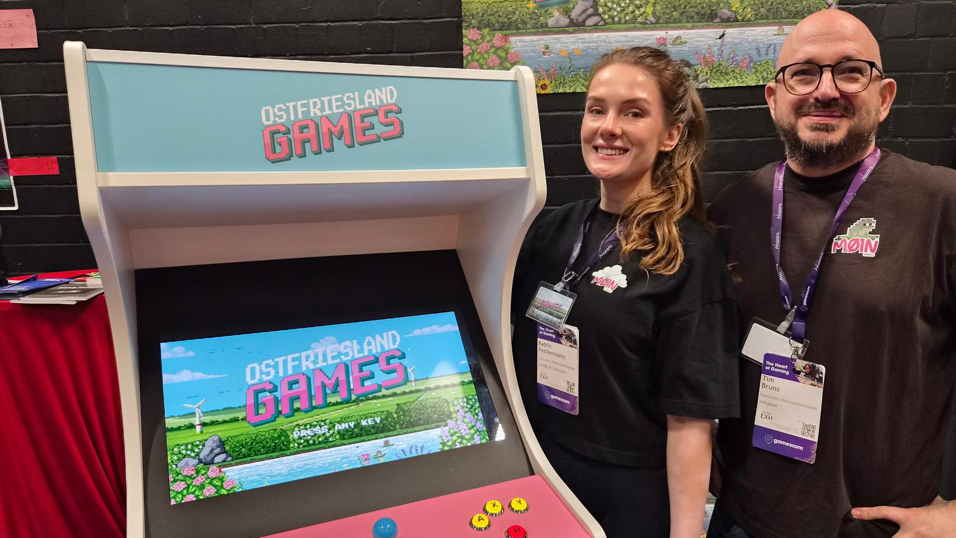 Ein Mann und eine Frau stehen neben einem Arcade Automaten mit der Aufschrift 