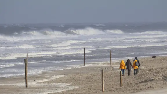 Bei stürmischem Wetter und Wellengang spazieren Spaziergänger am Strand der ostfriesischen Insel Norderney entlang. | picture-alliance/dpa, Volker Bartels Bei stürmischem Wetter und Wellengang spazieren Spaziergänger am Strand der ostfriesischen Insel Norderney entlang.