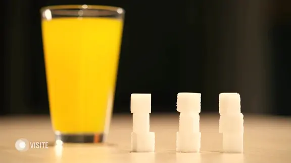 Neun Zuckerwürfel stehen neben einem Glas Limonade.