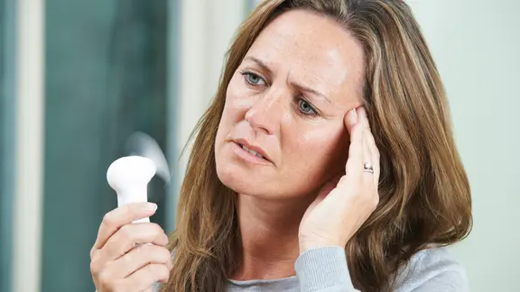 Frau schwitzt und hält sich Mini-Ventilator vors Gesicht