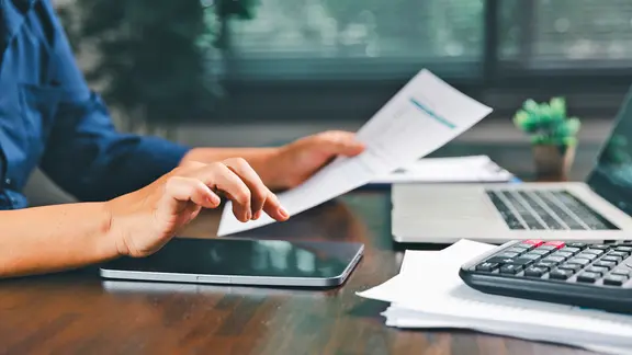 Eine Person sitzt an einem Tisch und stellt Berechnungen an. 