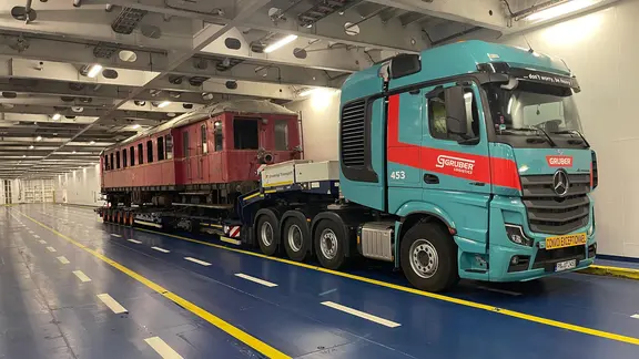 Der alte Triebwagen steht verladen auf einem Schwerlast-LKW im Unterdeck einer Ostsee-Fähre. So wurde das ramponierte Unikat von Dänemark zurück nach Deutschland gebracht.